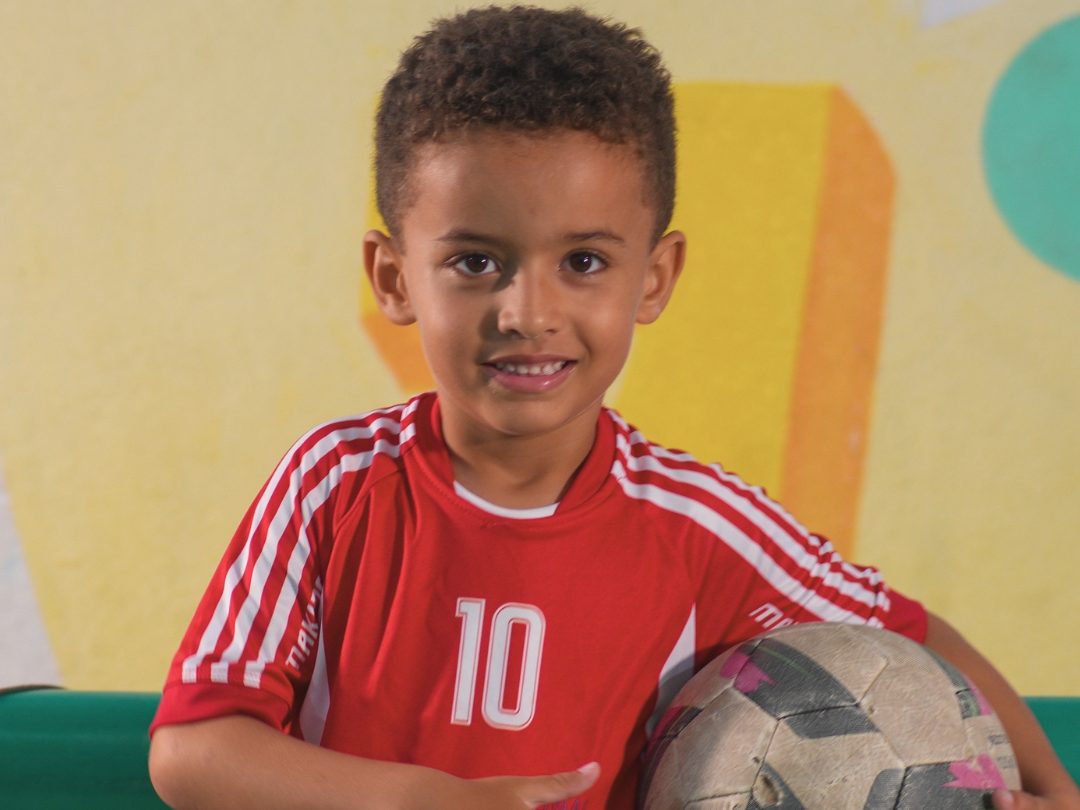Aluno da Erlach Kids uniformizado, segurando uma bola de futsal