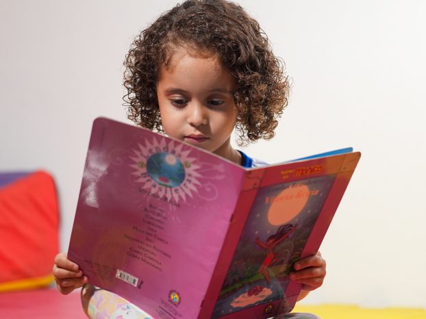 Aluna da Erlach Kids sentada no chão, folheando um livro ilustrado